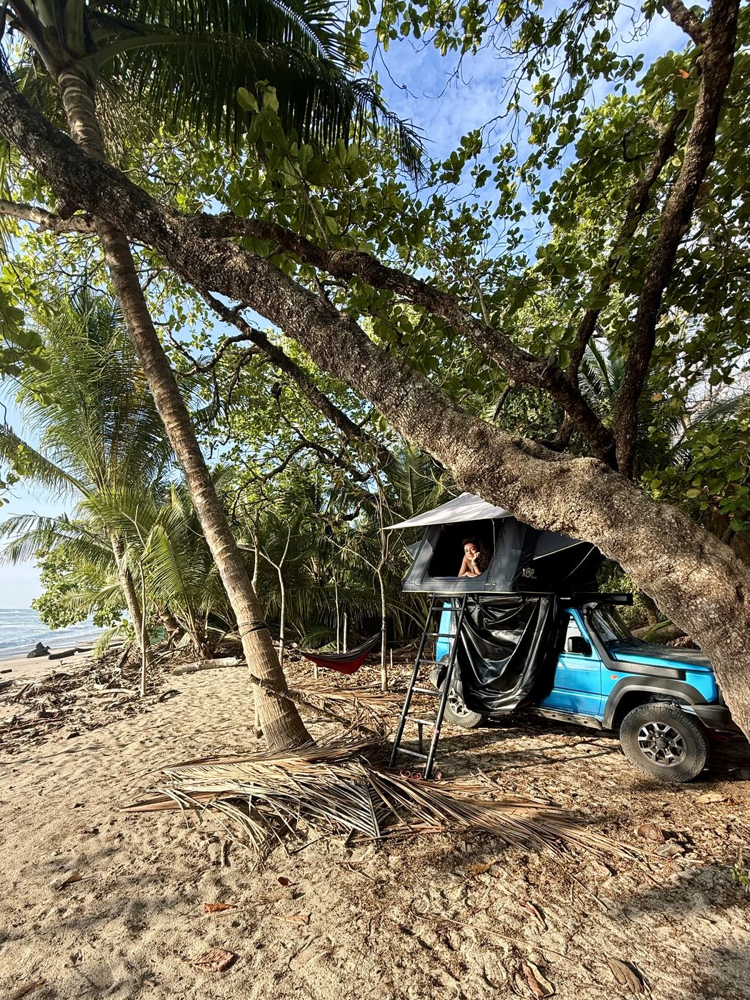 Blue Suzuki Jimny with its rooftop tent open on a beach