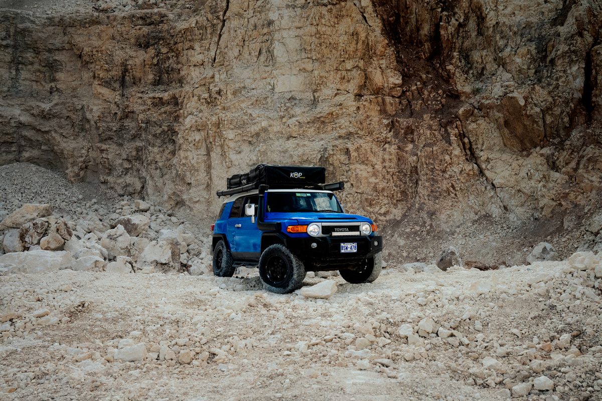 Blue Toyota FJ Cruiser on a gravel track below a rock wall