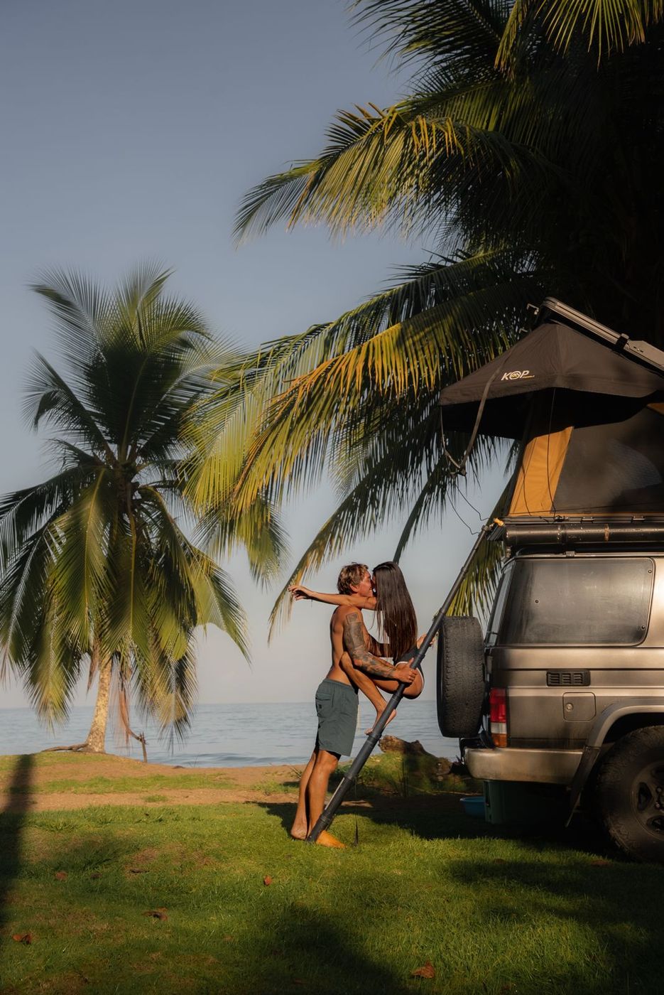 Couple beside a Toyota Land Cruiser LX under a palm tree at sunset
