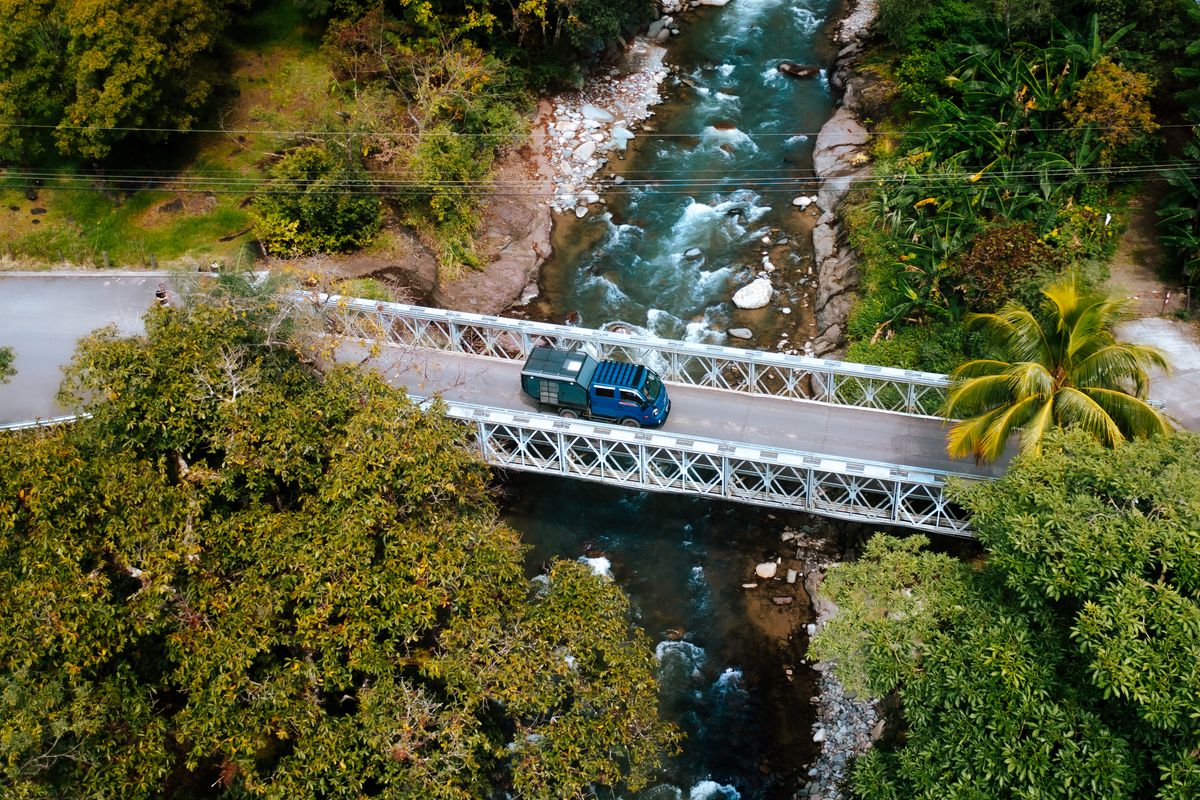 Kia Bongo 4x4 camper crossing a bridge over a jungle river, seen from above