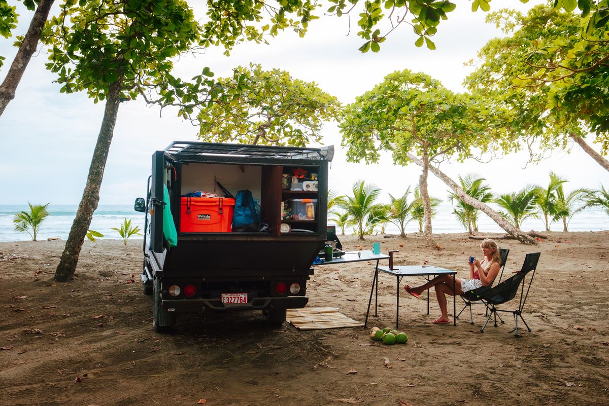Kia Bongo 4x4 camper open at the back on a beach, with a table and chairs set out