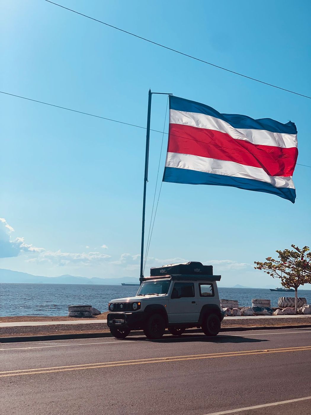 Suzuki Jimny driving below a Costa Rican flag on the coast