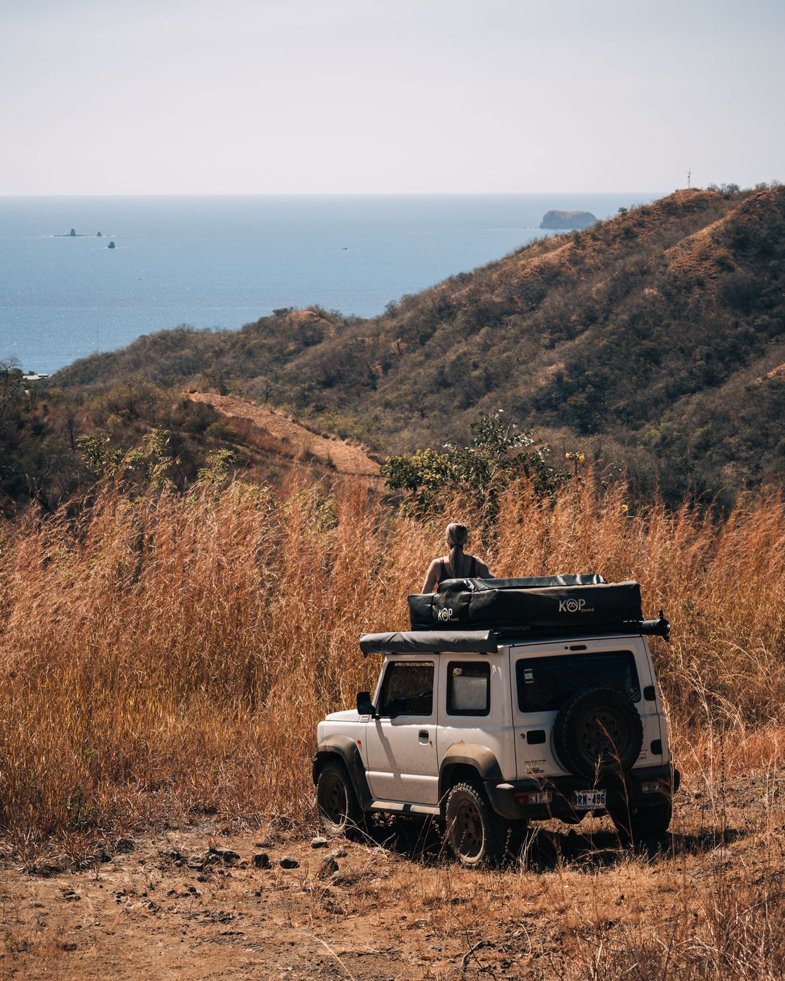 Suzuki Jimny parked on a dry hillside above the ocean