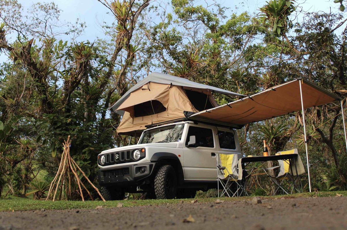 Suzuki Jimny with rooftop tent and side awning set up at a campsite