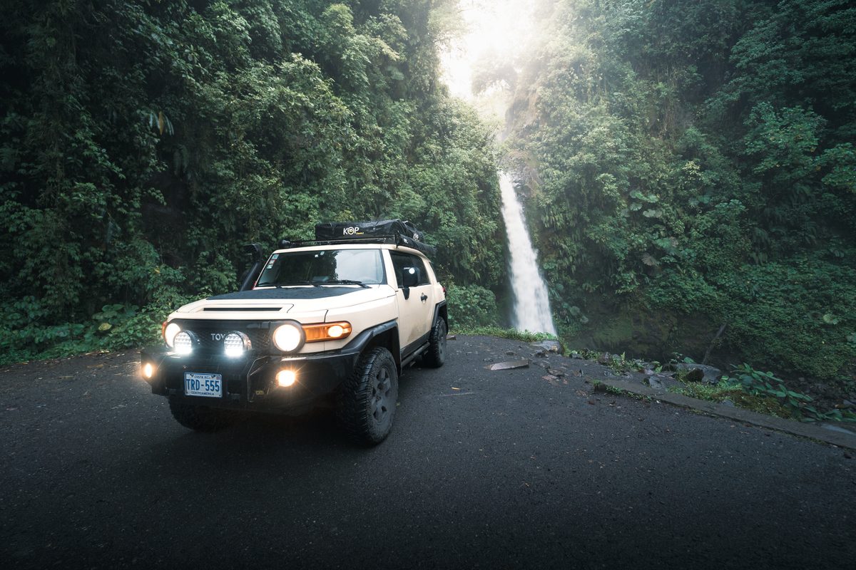 Toyota FJ Cruiser on a road below a waterfall