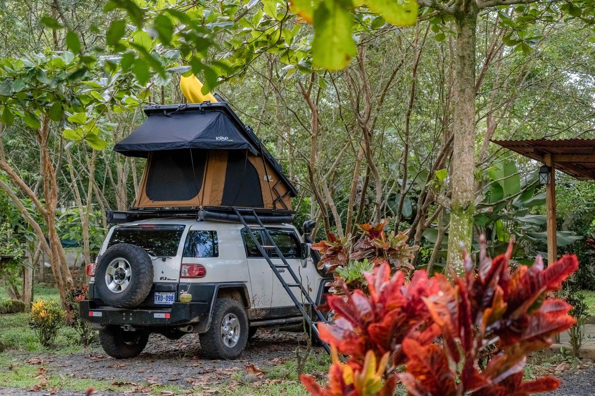 Toyota FJ Cruiser with a hard-shell rooftop tent open at a garden campsite