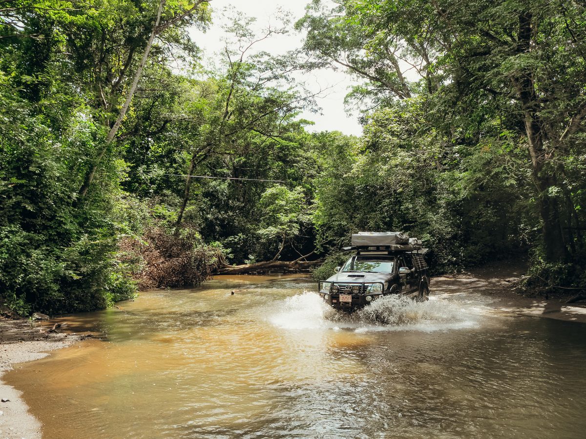Toyota Hilux driving through a shallow river on a jungle track
