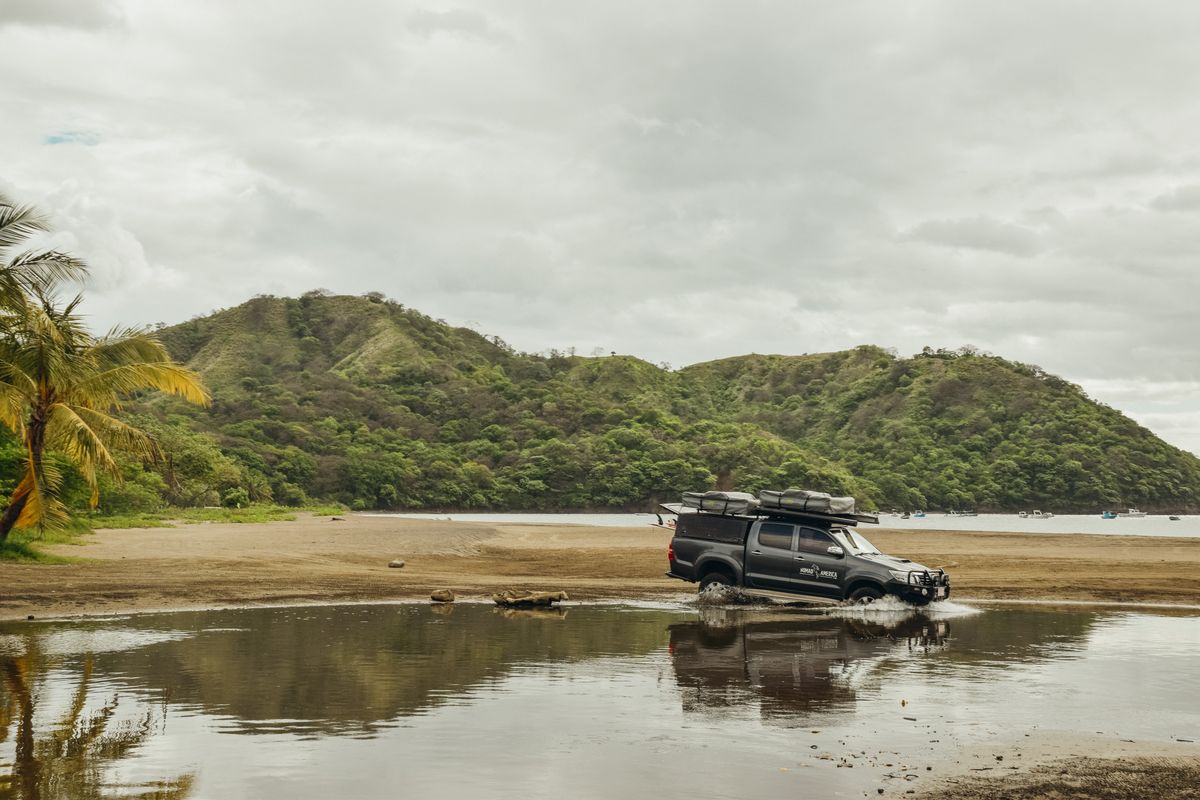 Toyota Hilux reflected in a lagoon below green hills