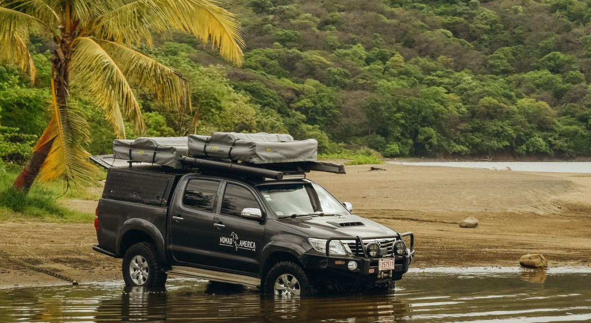 Toyota Hilux with a rooftop tent parked on a wide beach
