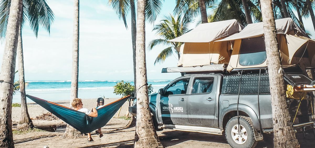 Toyota Hilux with two rooftop tents open on a palm beach, a hammock strung beside it