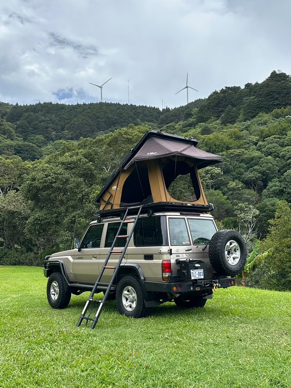 Toyota Land Cruiser LX with its rooftop tent open on a grassy hillside