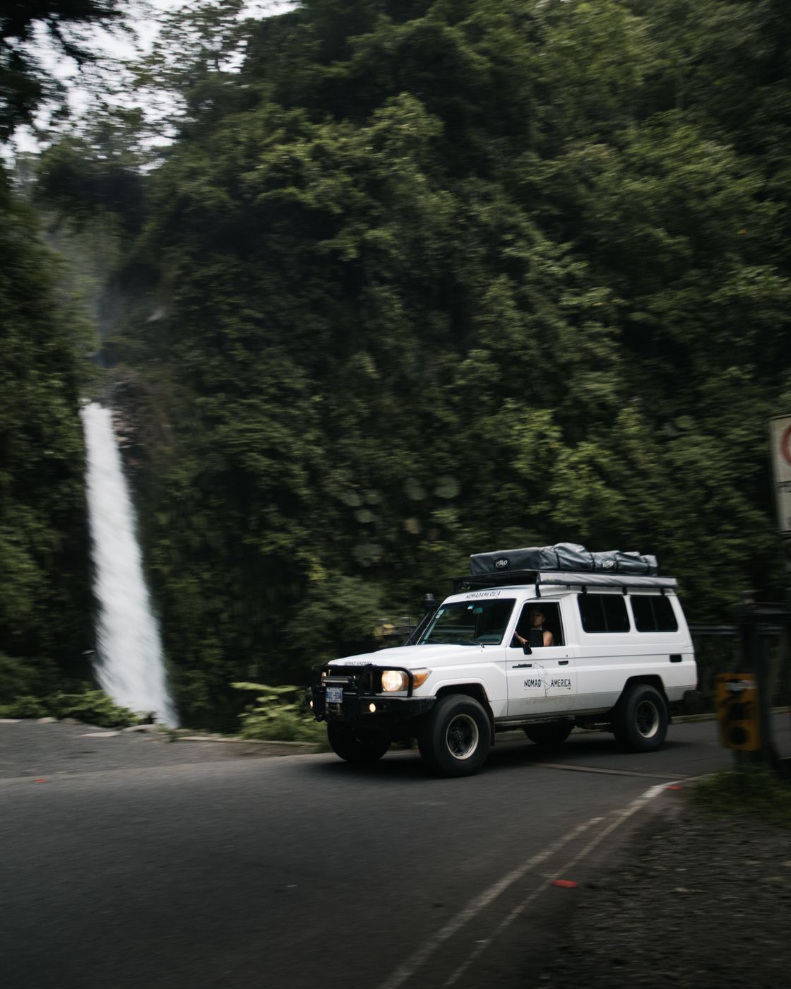 Toyota Land Cruiser Troopie on a road below a waterfall