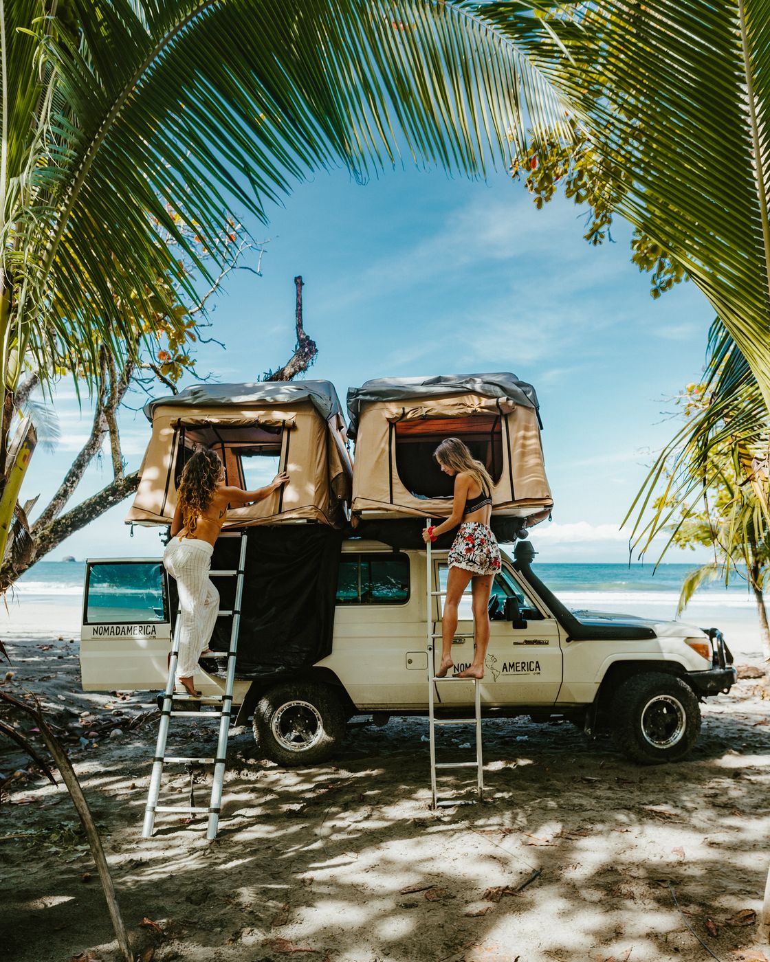 Toyota Land Cruiser Troopie with two rooftop tents open on a beach under palms