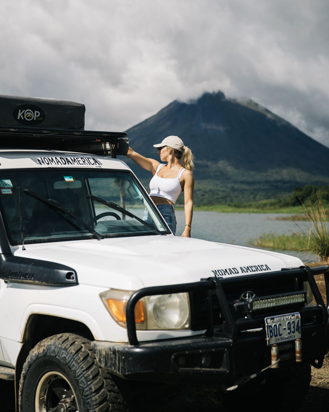 Traveler standing beside a Toyota Land Cruiser Troopie with a volcano behind
