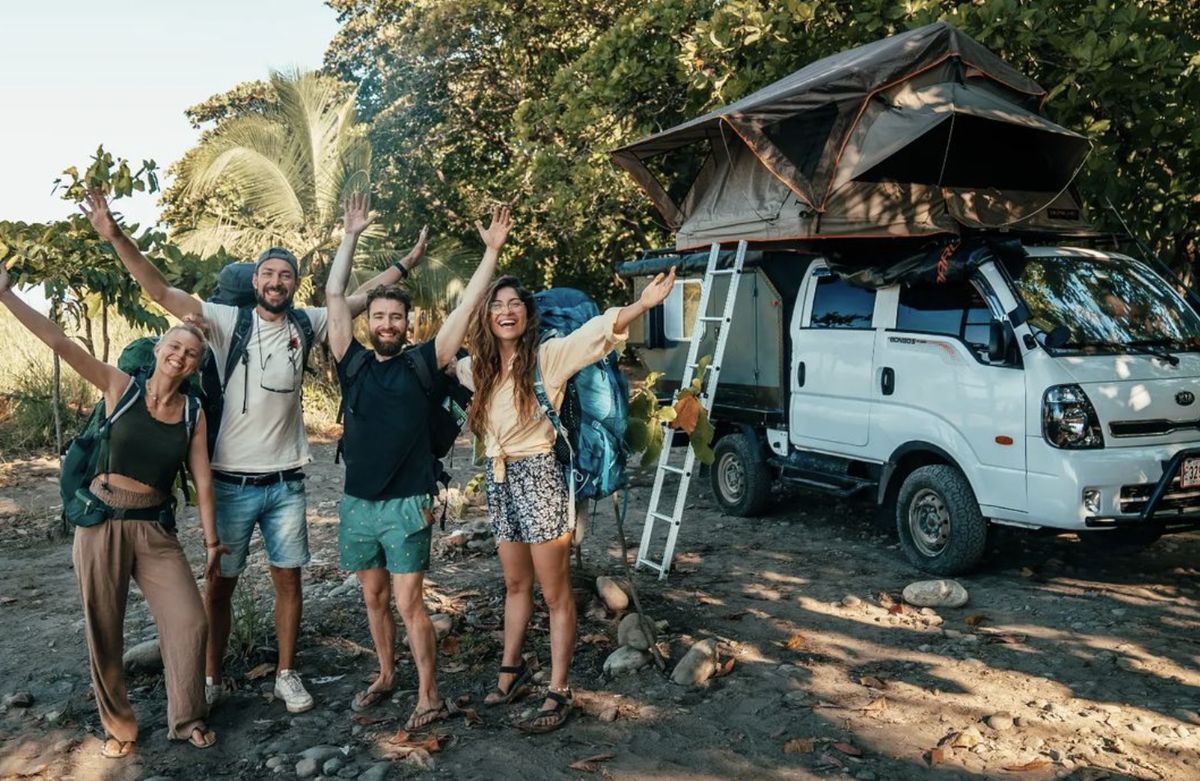 Travelers beside a Kia Bongo 4x4 camper with a rooftop tent open