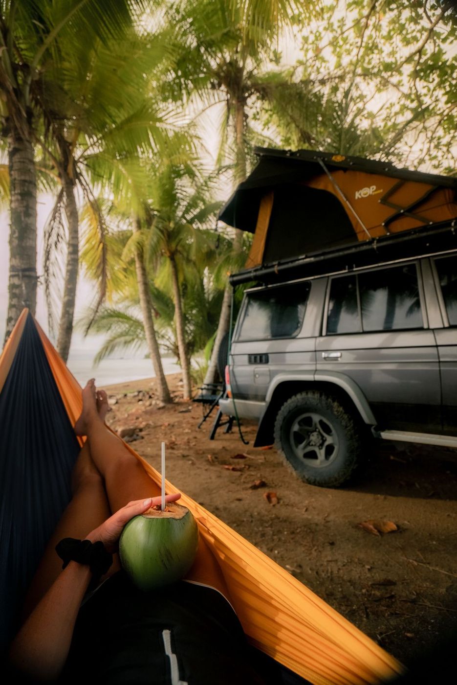 View from a hammock to a Toyota Land Cruiser LX with its rooftop tent open