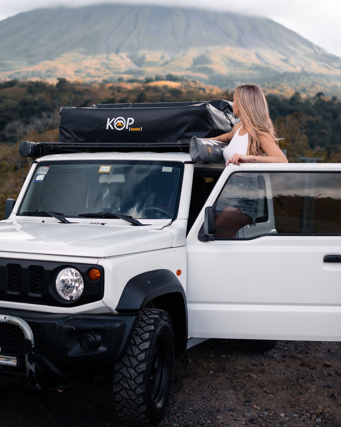 White Suzuki Jimny with a rooftop tent below a volcano
