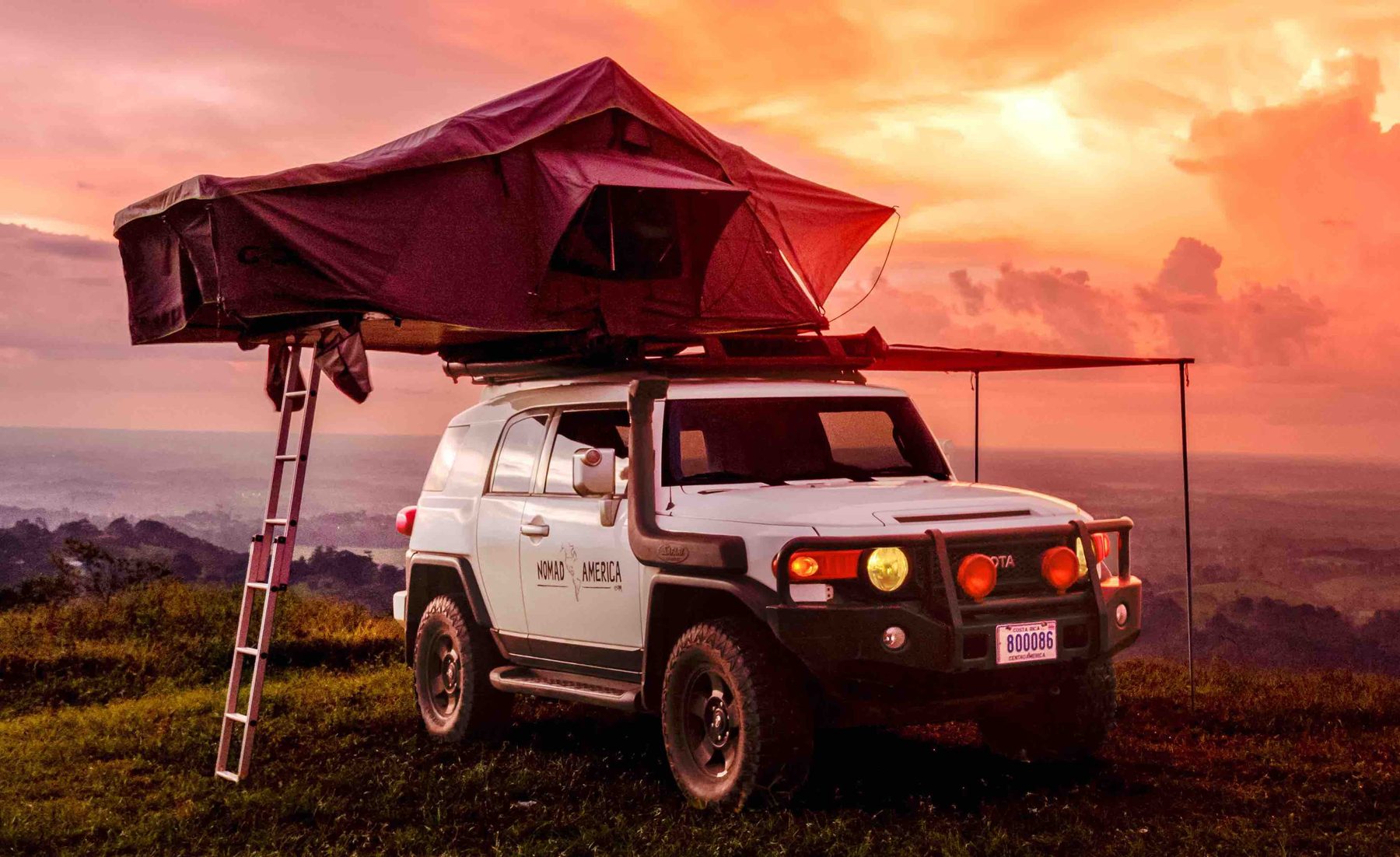 White Toyota FJ Cruiser 4x4 with a rooftop tent and side awning open at sunset in Costa Rica