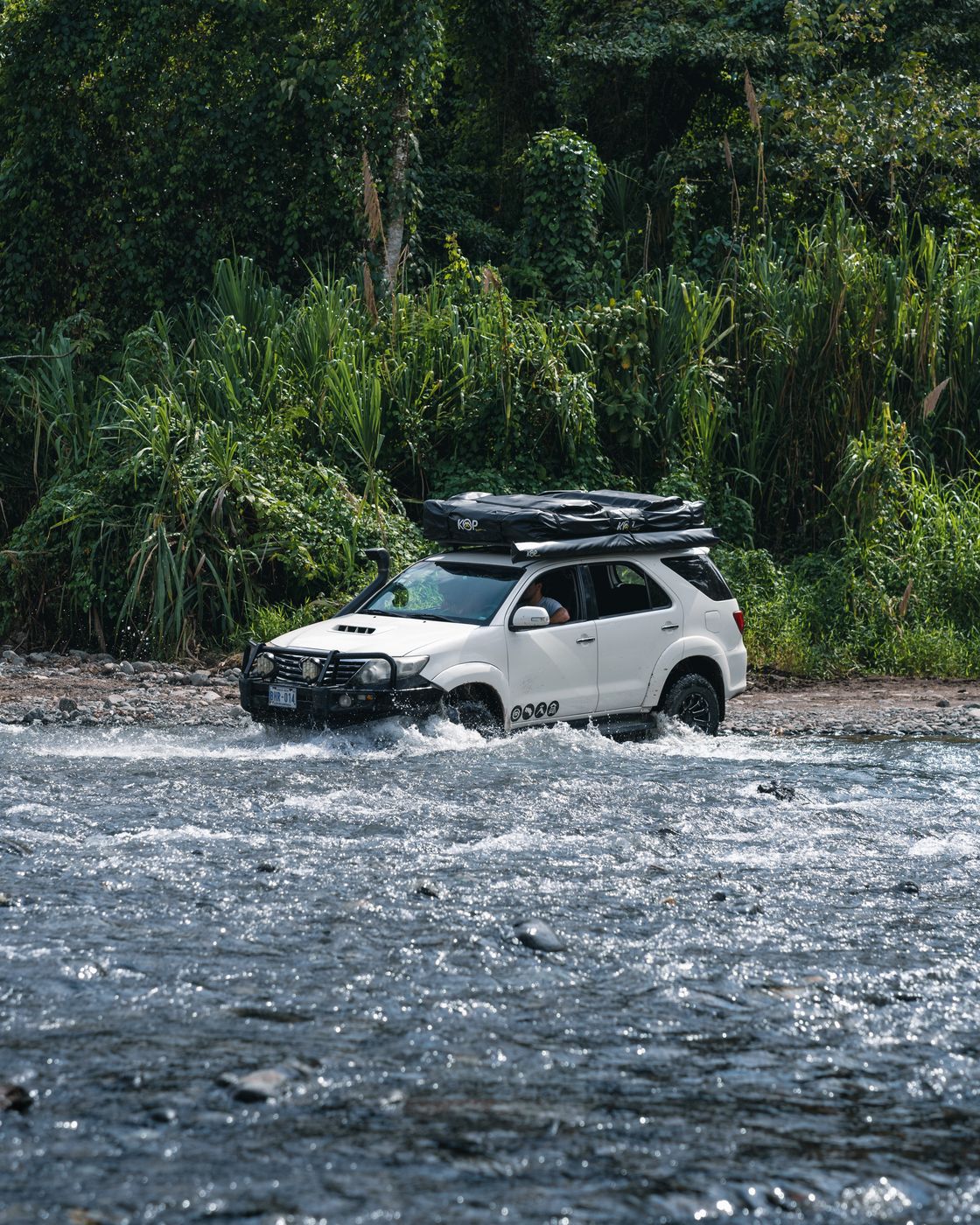 White Toyota Fortuner crossing a river in the rainforest